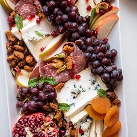 Pomegranate Jewel Cascade cheese board features vibrant colors with flowing cheeses and fruits.
