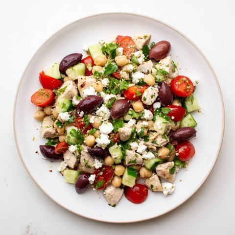 Gefüllte Schüssel mit mediterraner Hühnchen-Kichererbsen-Salat: Hühnchen, Feta, Oliven und Gurken mit Zitronen-Dressing garniert.