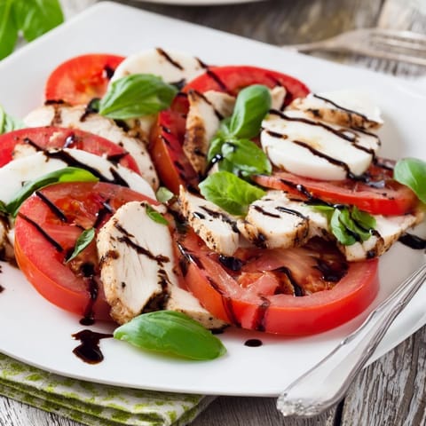 A juicy slice of grilled chicken breast rests on ripe tomato and creamy mozzarella.